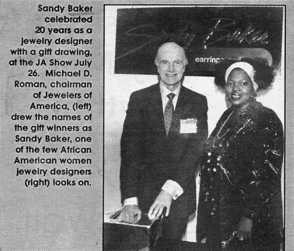 Sandy celebrated her 20th year in business at the JA Show on July 26, where Michael D. Roman, chairman of Jewelers of America, drew the names of the gift winners. One of the few African American women jewelry designers, she looked on.
